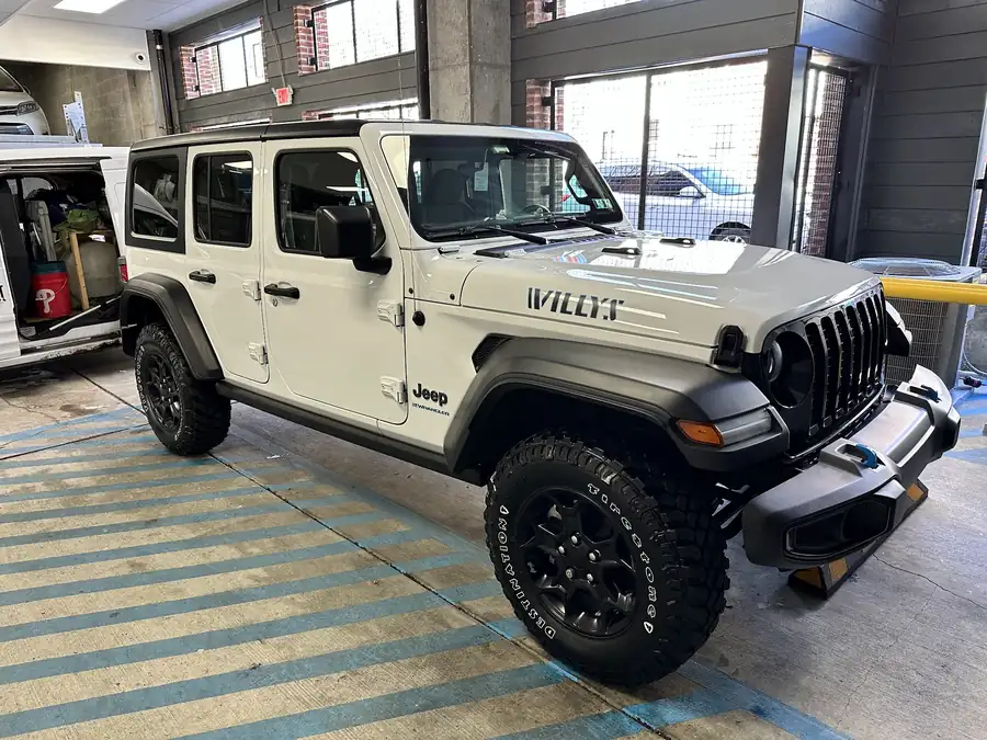 White Jeep Wrangler Willys, washed and dressed, beside the open side door of the detailing van